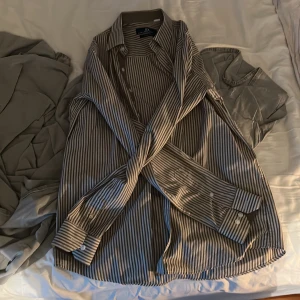 Randig skjorta från Rateb Safe Slim Fit - Säljer en snygg randig skjorta från Rateb Safe i slim fit-modell. Skjortan är beige och vit med klassisk krage, långa ärmar och knappar framtill. Perfekt för dig som gillar stilrena och moderna plagg. Passar dig som vill ha en skjorta med smalare passform.