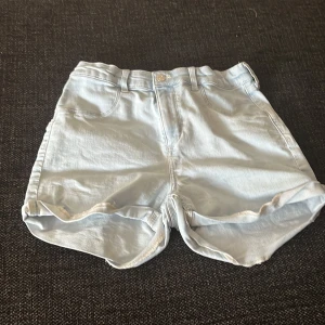 Ljusblå jeansshorts från H&M - Snygga ljusblå jeansshorts från H&M med klassisk femficksdesign och uppvikta benslut. Shortsen har bälteshällor och knappstängning framtill. Perfekta för varma dagar och enkel att matcha med allt i garderoben.