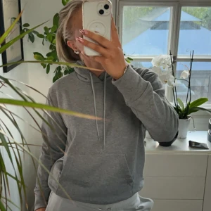 Grå hoodie med huva och snörning - Säljer en enkel och stilren grå hoodie med huva och snörning. Tröjan har en klassisk känguruficka framtill och är långärmad. Perfekt för dig som gillar en chill och avslappnad look.