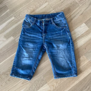 Blå jeansshorts från Lab Industries - Snygga blå jeansshorts från Lab Industries med klassisk femficksdesign och coola slitningar framtill. Shortsens längd går till knäna och de har detaljerade bakfickor, bälteshällor och dragkedja. Perfekta för en avslappnad och trendig look i sommar.