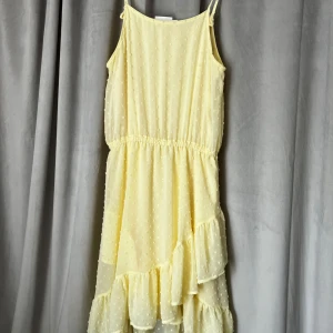 Ljusgul prickig volangklänning KappAhl - Superfin ljusgul klänning från KappAhl med tunna axelband och volanger nedtill. Prickigt mönster i tyget och elastisk midja för skön passform. Perfekt för sommarens alla tillfällen, lätt och luftig med härlig flow.