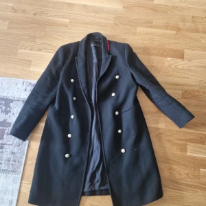 Svart rock från Zara Woman med knappar - Stilren svart rock från Zara Woman med dubbelknäppning i silverfärgade knappar. Klassisk krage och långärmad modell, perfekt för dig som gillar en tidlös look. Snygg passform och diskreta fickor framtill. Passar dig som vill ha en elegant och clean jacka. Är lite noprig därav priset.