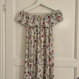 Blommig offshoulder långklänning - Säljer en superfin långklänning med offshoulder och volang upptill. Klänningen har ett ljust blommigt mönster.