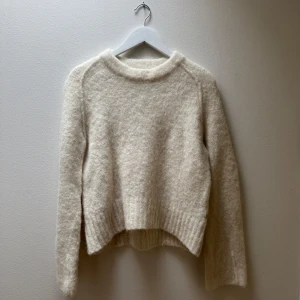 Beige stickad tröja Marc O'Polo Denim - Mysig vit/beige stickad tröja från Marc O'Polo Denim i storlek M. Tröjan har rund hals, lång ärm och är tillverkad av 40% alpaca, 31% polyamid, 25% ren ull och 4% elastan. Perfekt för dig som gillar en enkel och chill look med lite fluffig känsla.