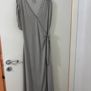 Svartvit omlott långklänning - Snygg svartvit långklänning med diagonala ränder och omlott-design. Aldrig använd 🌟storlek S men passar även M.
