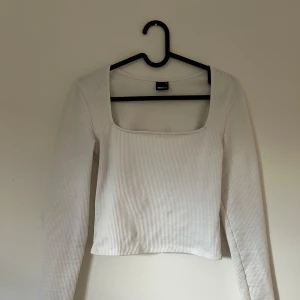 Vit ribbad topp från Gina Tricot - Vit långärmad topp från Gina Tricot med fyrkantig urringning och ribbad struktur. Lätt att matcha med andra plagg.