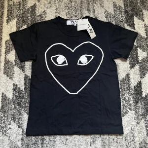 Svart CDG play t shirt - Svart t-shirt från Comme des Garçons Play med stort vitt hjärta och ögon tryckt på bröstet. Klassisk rund hals och korta ärmar. Perfekt för dig som gillar statement-plagg och coola prints.
