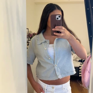 Ljusblå croppad kofta med knappar - Säljer en ljusblå croppad kofta med korta ärmar och snygga fransade kanter. Koftan har pärlemorknappar framtill och en klassisk krage. Perfekt för dig som gillar en elegant och trendig stil.