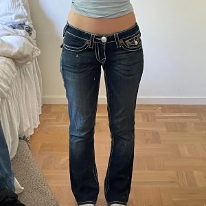 True Religion mörkblå bootcut jeans - Mörkblå jeans från True Religion med vita sömmar och ikoniska bakfickor med knapp och broderi. Låg midja och bootcut passform. De är vintage och storlek 27 i midajan. 