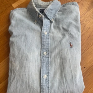 Ljusblå skjorta från Polo Ralph Lauren - Snygg ljusblå skjorta från Polo Ralph Lauren i slim fit-modell. Skjortan är i 100% bomull, har klassisk button down-krage, vita knappar och den ikoniska broderade loggan på bröstet. Perfekt för en clean och stilren look. Kan gå ner i pris vid snabb affär 😉
