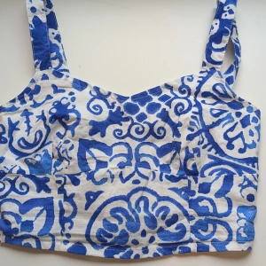 Blåvit linnetopp Holly & Whyte XS - Superfin blåvit linnetopp från Holly & Whyte med coolt abstrakt mönster. Toppen har breda axelband, smockad rygg och är gjord i mjuk ekologisk bomull. Perfekta för skol/jobb start🩷