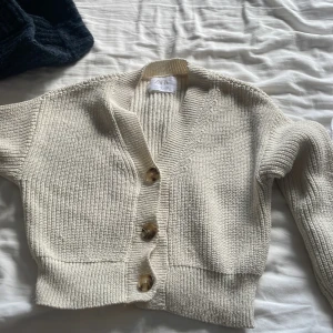 Beige stickad kofta från Zara - Säljer en beige stickad kofta från Zara med grov ribbstickning och tre stora knappar framtill. Koftan har v-ringad hals och långa ärmar, perfekt för lager på lager. Enkel och clean design som funkar till många olika stilar.