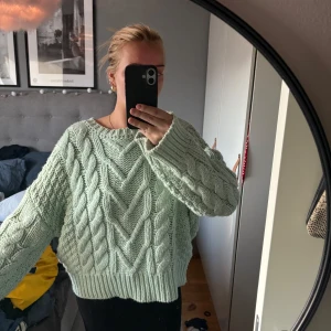 Ljusgrön stickad kabeltröja - Supermysig ljusgrön stickad tröja med grovt kabelmönster och breda ribbade muddar. Tröjan har en loose passform och långa ärmar, perfekt för att chilla eller hänga med kompisar. Färgen är fräsch och ger en soft vibe till din outfit.