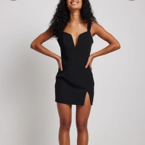 Svart kort klänning med slits - Snygg svart kort klänning med smala axelband och djup v-ringning. Klänningen har en liten slits framtill och figurnära passform, perfekt för en trendig look i sommar till till exempel fest eller festival, den är är från nakd och helt slut på hemsidan, klänningen är även i storlek 36 och endast använd 1 gång hör av dig vid frågor eller funderingar