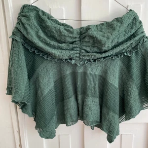 Grön volangkjol från Urban Outfitters - Säljer en grön kortkjol från Urban Outfitters med volangdetaljer och vågig struktur. Den är väldigt stretchiga så passar M också. Perfekt för dig som gillar lågmidjade kjolar. Använt en gång 🍐