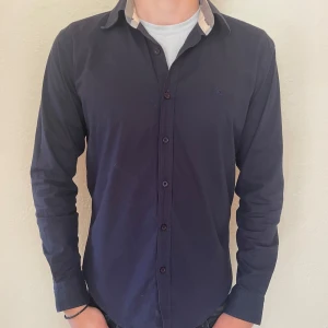 Burberry skjorta  - Säljer en stilren mörkblå skjorta från Burberry. Säljer den pågrund av att jag har vuxit ur den. Skjortan är i storlek M. 