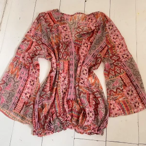 Bohemisk boho Mönstrad blus i rosa och rött - Färgglad blus med vida ärmar och elastisk nederkant. Blusen har ett bohemiskt mönster i rosa, rött, orange och beige med inslag av blommor och geometriska former. Perfekt för dig som gillar unika plagg med mycket färg.