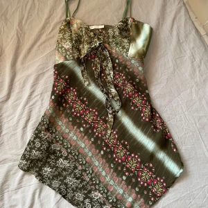 Somrig topp - Supersöt topp i glansigt grönt tyg med blommigt mönster. Finns justerbara band. Luftigt material vilket gör den perfekt för sommaren! 