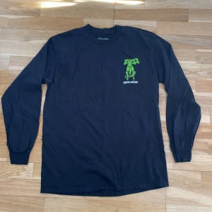 Svart långärmad tröja från Fucking Awesome - Säljer en svart långärmad tröja från Fucking Awesome med tryck av en grön tvåhövdad hund på bröstet och ryggen. Tröjan är i 100% bomull.