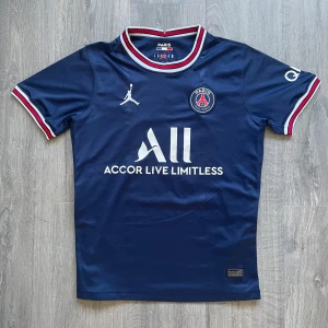 PSG Neymar Jr 10 matchtröja - Mörkblå Paris Saint-Germain fotbollströja med Neymar Jr och nummer 10 på ryggen. Tröjan har vita och röda detaljer vid krage och ärmslut, samt PSG-logga och Jordan-logga på bröstet. Materialet är glansigt och snabbtorkande.