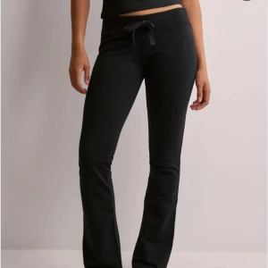 Svarta mjukisbyxor från Nelly  - Svarta mjukisbyxor med bootcut och dragsko i midjan. Byxorna har en bekväm passform och är perfekta för en avslappnad stil. Tillverkade i mjukt material som känns skönt mot huden.