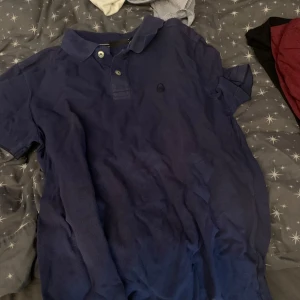 Mörkblå pikétröja från sail racing - Säljer en mörkblå pikétröja från sail racing  med klassisk krage och knappar framtill. Tröjan har korta ärmar och en diskret logga broderad på bröstet. Perfekt för en stilren och avslappnad look.