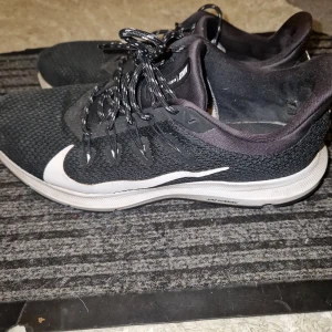 Svarta Nike löparskor med vit sula - Säljer ett par svarta Nike löparskor med vit sula och stor vit swoosh på sidan. Skorna har snörning och ovandel i mesh för bra ventilation. Perfekta för löpning eller träning.