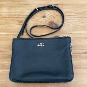 Svart axelväska från Zadig & Voltaire - Säljer min jättefina svarta axelväska i skinn från Zadig & Voltaire med silverfärgad logga framtill. Väskan har två fack med dragkedja och en justerbar axelrem. Dragkedjan på utsidan är i guld, silver och mässingfärger och insidan har ett guldfärgat foder som ger en cool och fin kontrast. Har små märken av användning men fortfarande i gott skick! Pris kan diskuteras vid snabb affär! 🌸