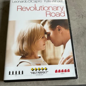Revolutionary Road - DVD med filmen Revolutionary Road med Leonardo DiCaprio och Kate Winslet i huvudrollerna. Omslaget är vitt med röd text och visar ett närbildsfoto på huvudkaraktärerna. Filmen är på svenska och har extramaterial som kommentarspår och bortklippta scener. Inplastad