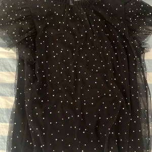 Svart och glittrig blus 💫 - Säljer en svart klänning med vita prickar och stora puffärmar i transparent tyll. Klänningen har en luftig passform och är perfekt för dig som vill sticka ut med ett lekfullt mönster. Supersöt och trendig modell!