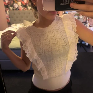 Vit volangtopp från Holly & Whyte - Supersöt vit topp från Holly & Whyte med volangdetaljer längs axlarna och broderade spetskanter.  Knappt använd!!!!!