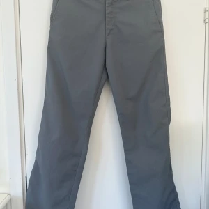 Grå chinos med raka ben - Säljer ett par stilrena grå chinos från Crocker med raka ben och klassiska fickor fram och bak. Byxorna har hällor för bälte och stängs med dragkedja och knapp. Perfekta för en clean och enkel look.