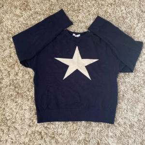 Mörkblå stickad tröja med stjärna från Gina Tricot - Mysig mörkblå stickad tröja från Gina Tricot med en stor vit stjärna på bröstet. Tröjan har lång ärm och rund halsringning. Perfekt för dig som gillar enkel men snygg design.