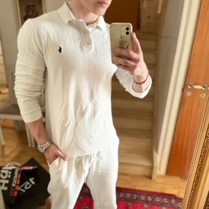 Vit pikétröja från Polo Ralph Lauren - Säljer en klassisk vit långärmad pikétröja från Polo Ralph Lauren. Tröjan har krage, knappar vid halsen och den ikoniska broderade loggan på bröstet. Slim fit-modell som sitter snyggt på kroppen.