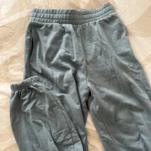 Grå mjukisbyxor med resårmidja - Mysiga grå mjukisbyxor med resår i midjan och sidofickor. Perfekta för chill dagar eller när du vill vara extra bekväm. Klassisk passform och mjukt material.