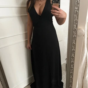 Svart långklänning med öppen rygg och smala axelband - Säljer en elegant svart långklänning med djup v-ringning och smala axelband. Klänningen har en snygg öppen rygg med korsade band.Perfekt för fest eller bal. Den är för lång på mig (156cm)!