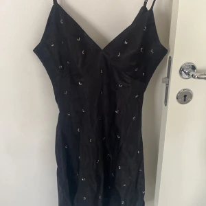Svart klänning med pärldetaljer från Zara - Säljer en svart kortklänning från Zara med smala axelband och v-ringning. Klänningen har små pärldetaljer över hela tyget och en figurnära passform. 