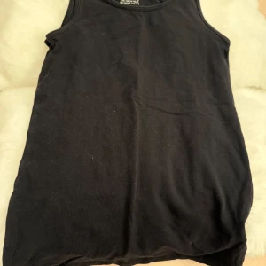 Svart linnetopp från H&M Basic - En enkel svart linnetopp från H&M Basic i mjuk bomull. Klassisk rund halsringning och ärmlös design, perfekt att bära som basplagg eller under andra kläder.