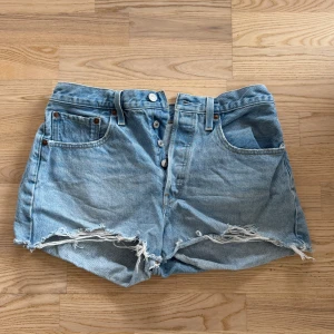 Ljusblå jeansshorts från Levi's 501 - Säljer ett par ljusblå jeansshorts från Levi's 501 med låg midja, fransiga benslut. Shortsen har knäppning framtill och den ikoniska läderpatchen bak. Perfekta för sommaren! Storlek 38/M och har i mycket bra skick🩷Nypris 799kr. 