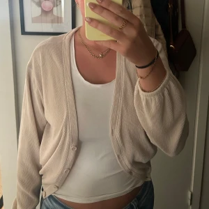 Beige ribbad kofta - Säljer en beige kofta med ribbad struktur och långa ärmar. Koftan har en avslappnad passform och knäpps framtill med två knappar. Perfekt att slänga över ett linne eller t-shirt för en chill look.