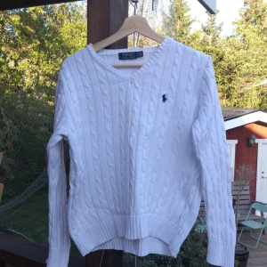 Vit stickad tröja från Polo Ralph Lauren - Vit kabelstickad tröja från Polo Ralph Lauren med v-ringning och broderad marinblå logga på bröstet. Klassisk och stilren modell med långa ärmar och ribbade muddar. Perfekt för lager-på-lager under kyligare dagar. Kontakta mig om du skulle ha några funderingar, pris kan diskuteras 