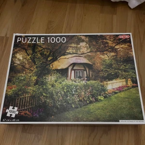 English Cottage in the Woods - 1000-bitar pussel - Pussel med 1000 bitar från Tactic med motiv av en engelsk stuga omgiven av grönska och blommor. Färgerna går i grönt, brunt och inslag av lila och rosa. Färdig storlek är 67 x 48 cm. Perfekt för dig som gillar utmanande pussel och idylliska landskap. Öppnad men inte använd 