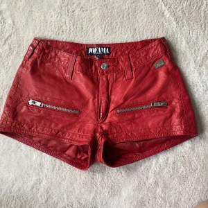 Röda skinnshorts  - Snygga röda shorts i läder från Jofama by Kenza. Modellen är kort med låg midja och har två dragkedjor framtill som detaljer. Säljer då de inte passar. Kontakta för midjemått.