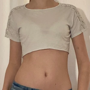 Vit croppad topp med spetsdetaljer - Säljer en vit croppad topp med korta ärmar och fina spetsdetaljer på axlarna. Toppen har en rund halsringning och är tillverkad i mjukt material. Perfekt för en trendig och avslappnad look.💗💗