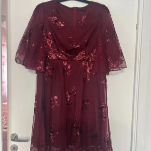 Vinröd paljettklänning från SHEIN Curve - Säljer en vinröd långklänning från SHEIN Curve med glittriga paljettdetaljer och transparenta vida ärmar. Klänningen har blommigt mönster och dragkedja i ryggen. Perfekt för festliga tillfällen!