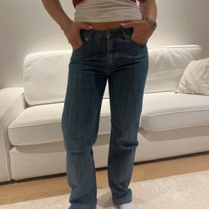 Blå raka jeansbyxor - Säljer ett par klassiska blå jeansbyxor med normal passform och raka ben. Jeansen har fem fickor, bälteshällor och stängs med dragkedja och knapp. Perfekta till vardags och lätta att matcha med olika toppar.
