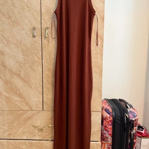 Rostbrun ribbad långklänning - Säljer en ärmlös långklänning i rostbrun färg med ribbad struktur. Klänningen har smala axelband och elastisk tyg, vilket kan fungera som size S-M.