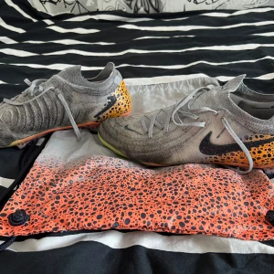 Nike grå-orange fotbollsskor med mönster - Snygga grå fotbollsskor från Nike med svart swoosh och coolt orange och svart prickigt mönster på hälen och sulan. Skorna har snörning och stickad ovandel för skön passform. Sulan har detaljer i gult och orange. PRIS KAN DISKUTERAS 