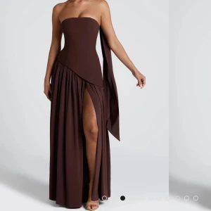 Babyboo klänning  - Säljer en brun axelbandslös långklänning med asymmetrisk överdel och slits framtill, sjal ingår. Klänningen är använd 1 gång och är i bra skick. Nypris 1977kr. 