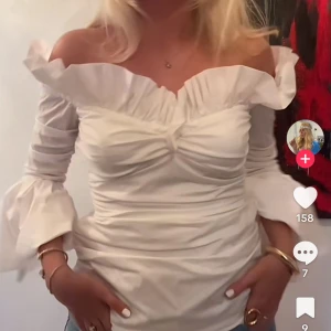 SÖKER Vit offshoulder blus med volang - Söker Supersöt vit offshoulder blus med volangkant längs axlarna och rynkade detaljer över bysten. Ärmarna är långa och avslutas med breda volanger för en extra romantisk vibe. Perfekt att styla med jeans eller kjol för en trendig look.